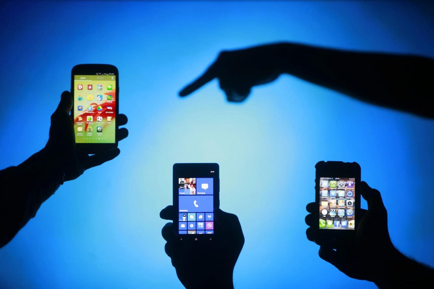 Men are silhouetted against a video screen as they pose with Samsung Galaxy S3, Nokia Lumia 820 and iPhone 4 smartphones (L-R) in this photo illustration taken in the central Bosnian town of Zenica, May 17, 2013. REUTERS/Dado Ruvic (BOSNIA AND HERZEGOVINA - Tags: BUSINESS TELECOMS) - RTXZQ6G