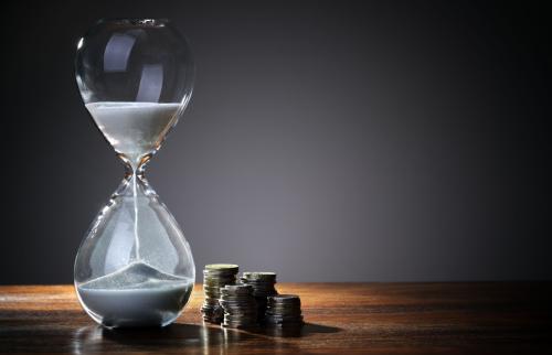 An hourglass on a table next to a stack of coins.