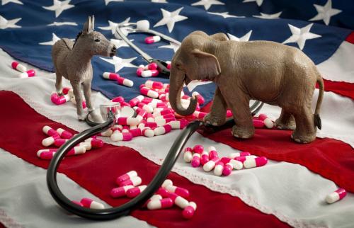 Donkey and elephant figures on an American flag covered in pills and a stethoscope.