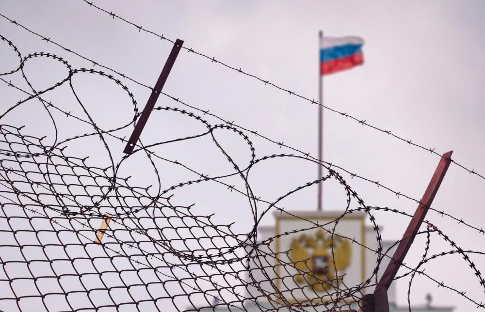 Building with Russian flag behind a barbed wire fence.
